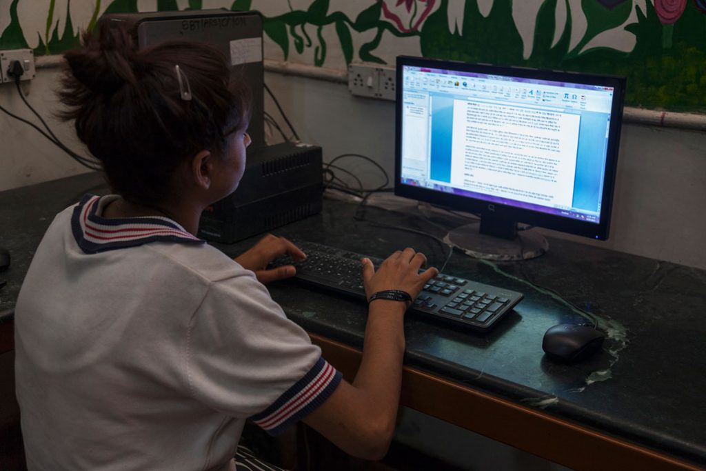 Intérieur couleur. Maison de Saalam Balaak Trust. Une jeune fille travaille sur un fichier word. L'ordinateur est posé sur une table devant elle.