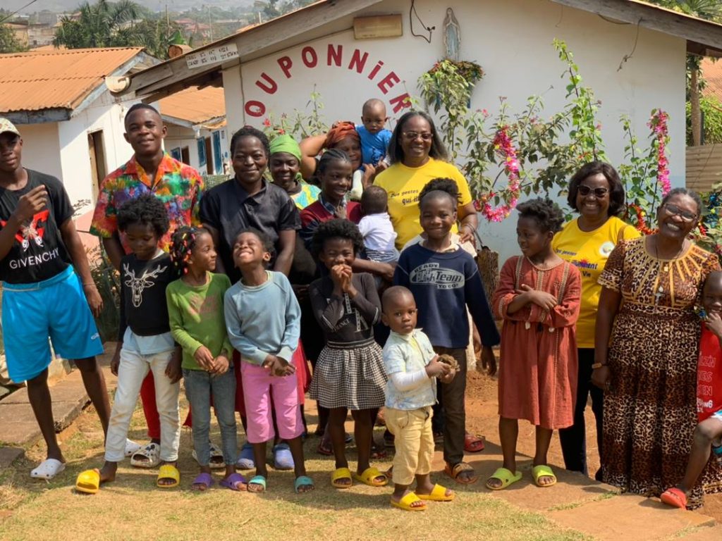 une quinzaine d'enfants âgés de 3 à 10 ans accompagnés de quelques adultes posent devant un bâtiment de la Pouponnière de Saint Kisito.