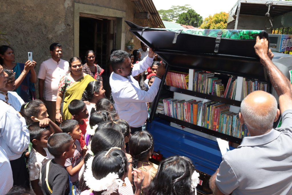 la partie arrière du tuk tuk est ouverte et dévoile des étagères de livres. des enfants entourent le tuk tuk